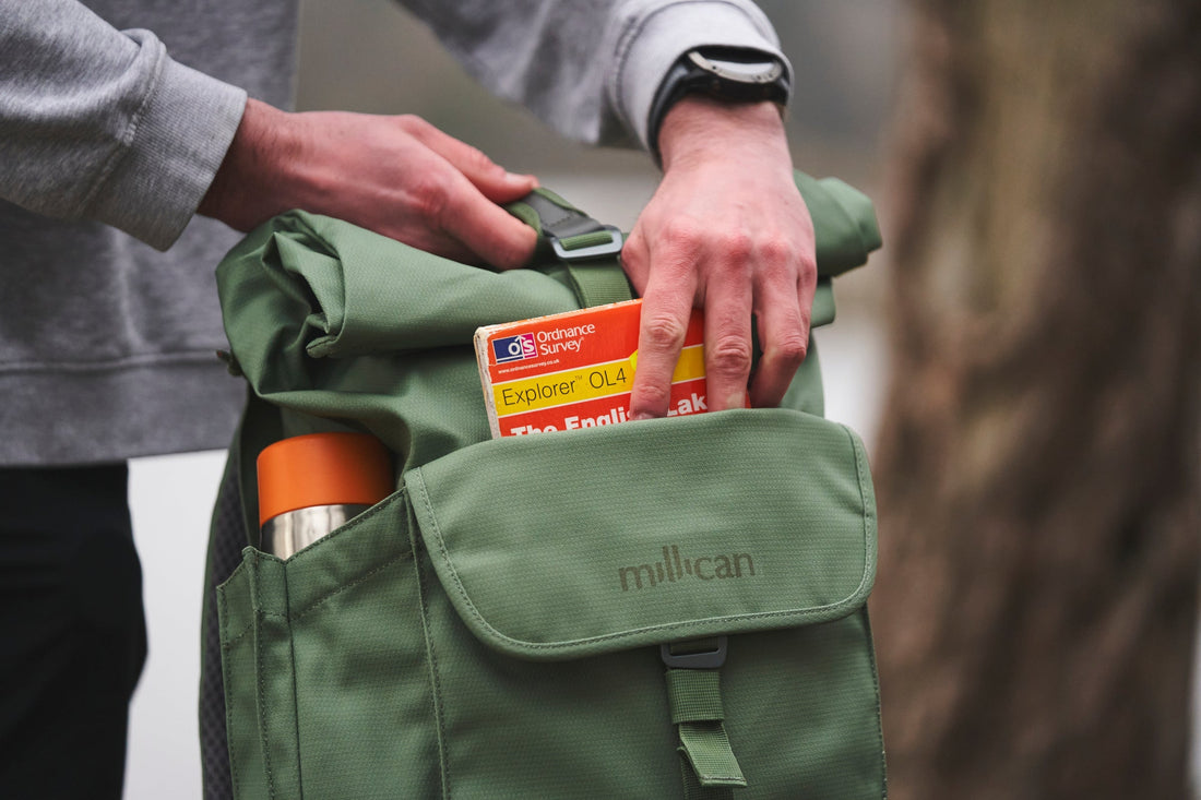 Hand placing a map into a green Millican backpack