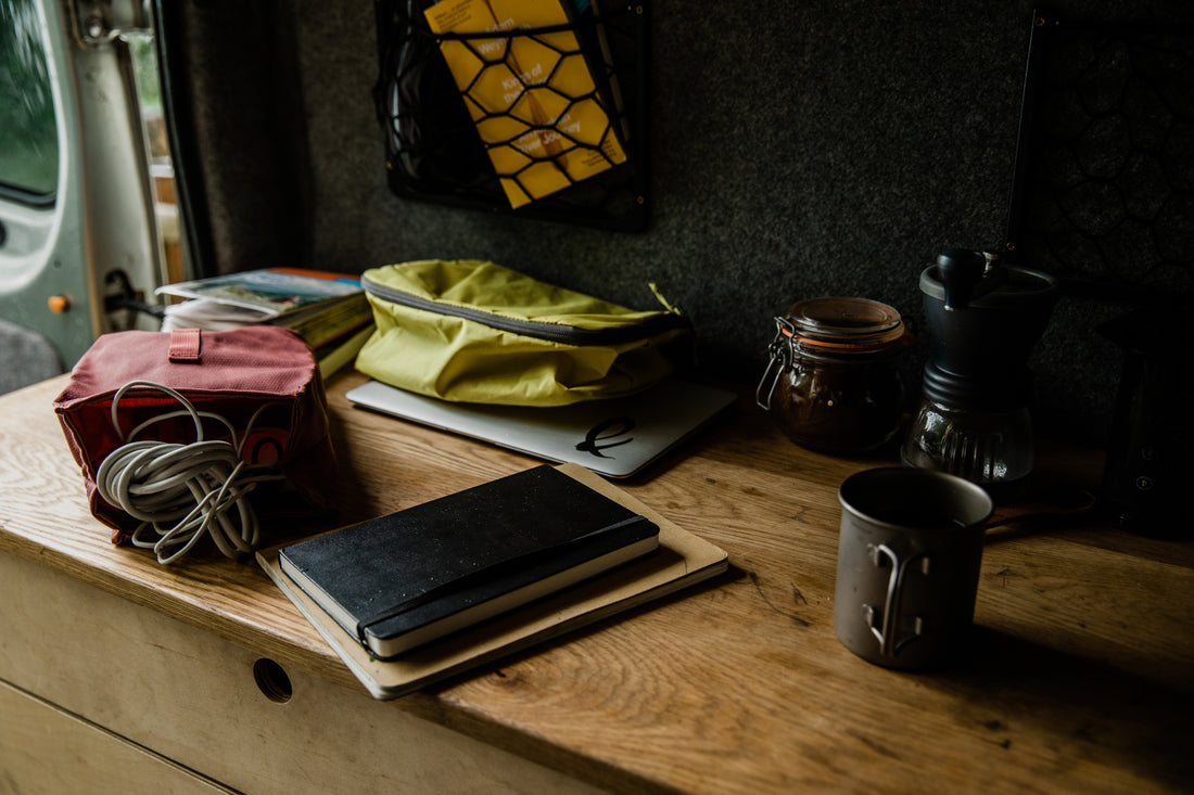 A tidy campervan workspace with pouches, notebooks, and a coffee setup