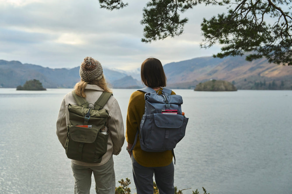 Two people wearing Millican Smith The Roll Top bags overlooking a lake