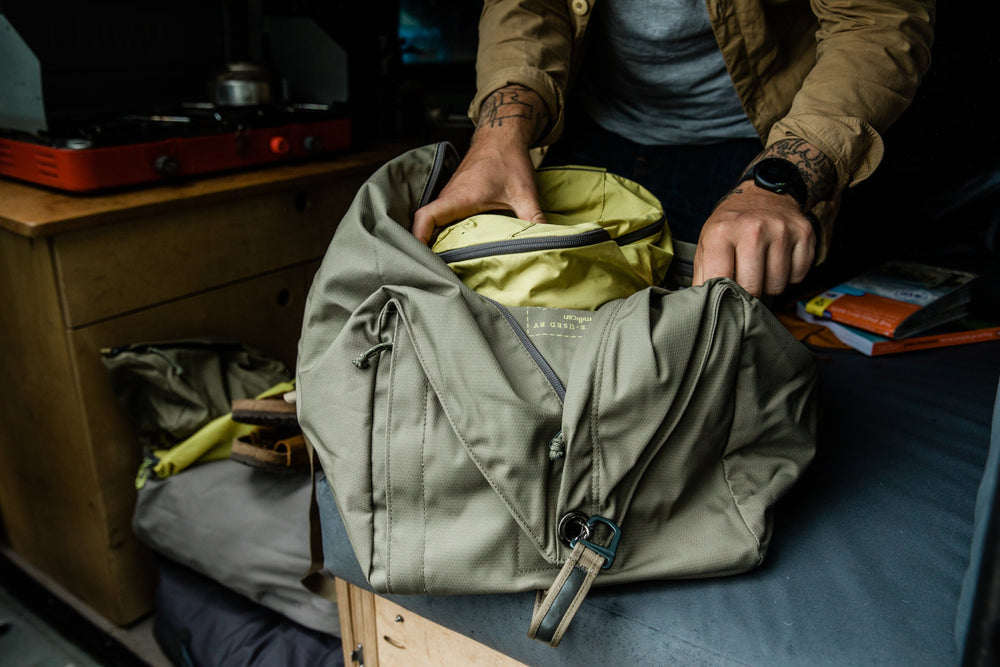 Person packing clothes into a green backpack on a table indoors