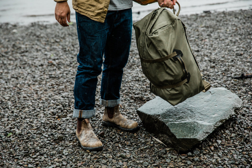 Person carrying a heavy duffel bag on a rocky beach