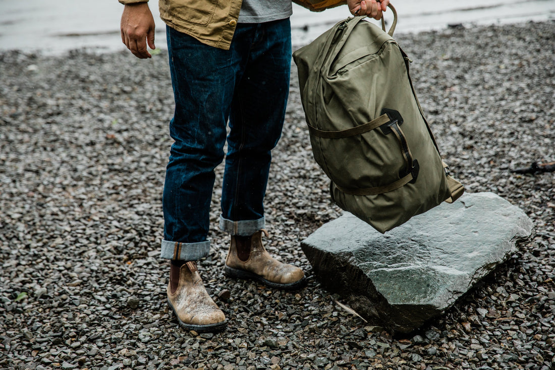 Person carrying a heavy duffel bag on a rocky beach