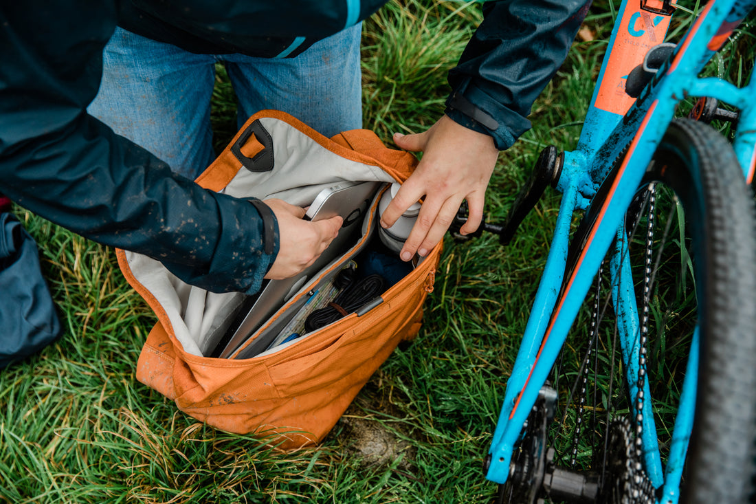 A person organising items in an orange Millican bag next to a blue bicycle