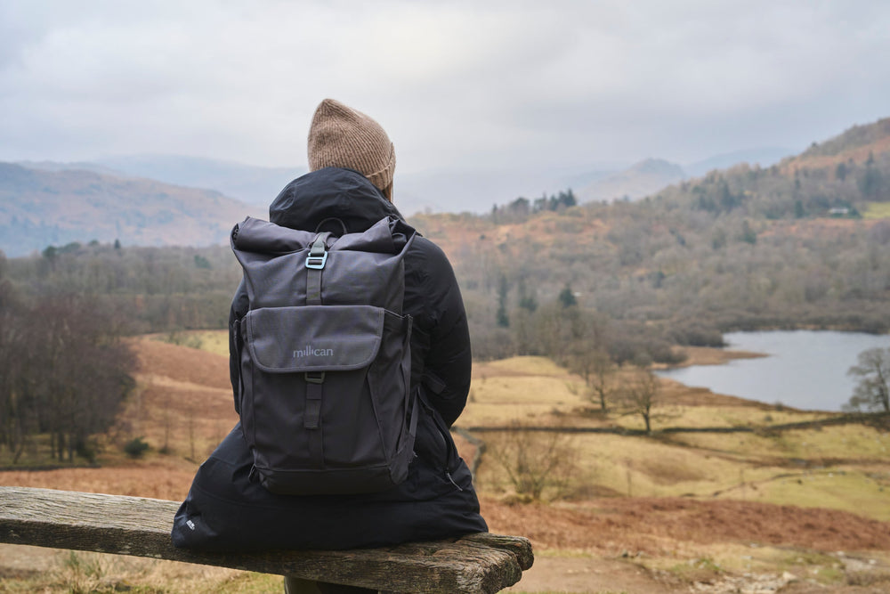 Person with a backpack sitting on a bench overlooking a lake and mountains