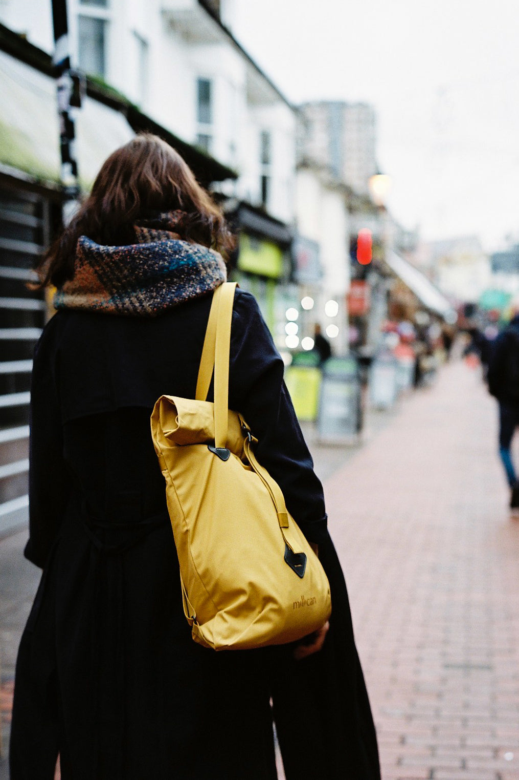 Person walking on a street with a yellow Millican backpack