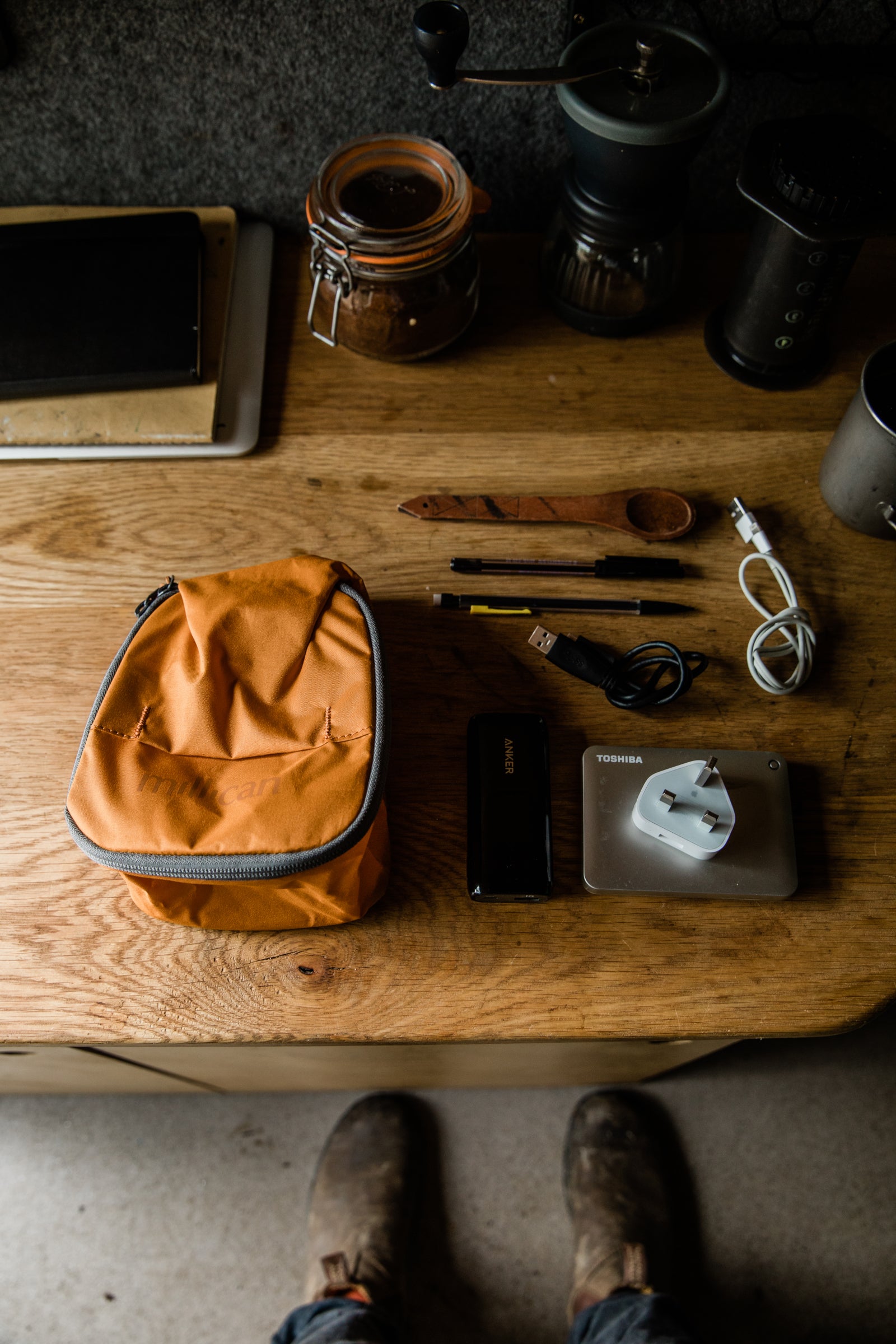 An orange Millican bag and various small items neatly arranged on a wooden table