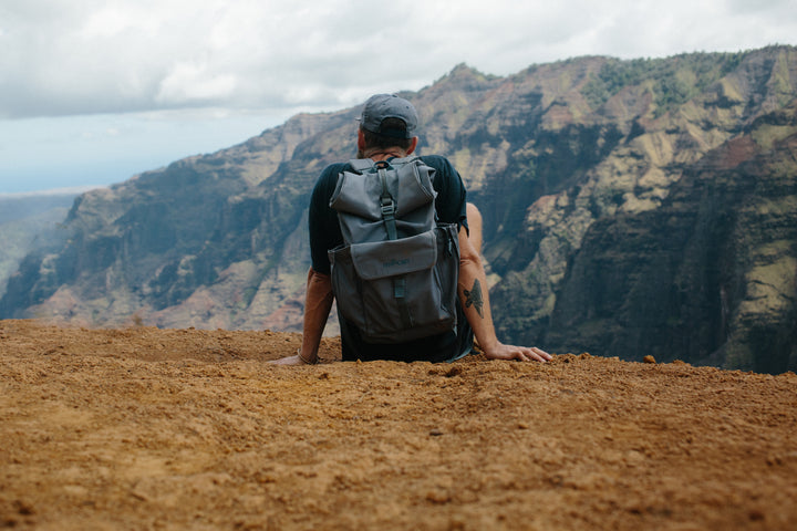A person wearing a Millican backpack, sitting on a mountain edge overlooking a dramatic canyon
