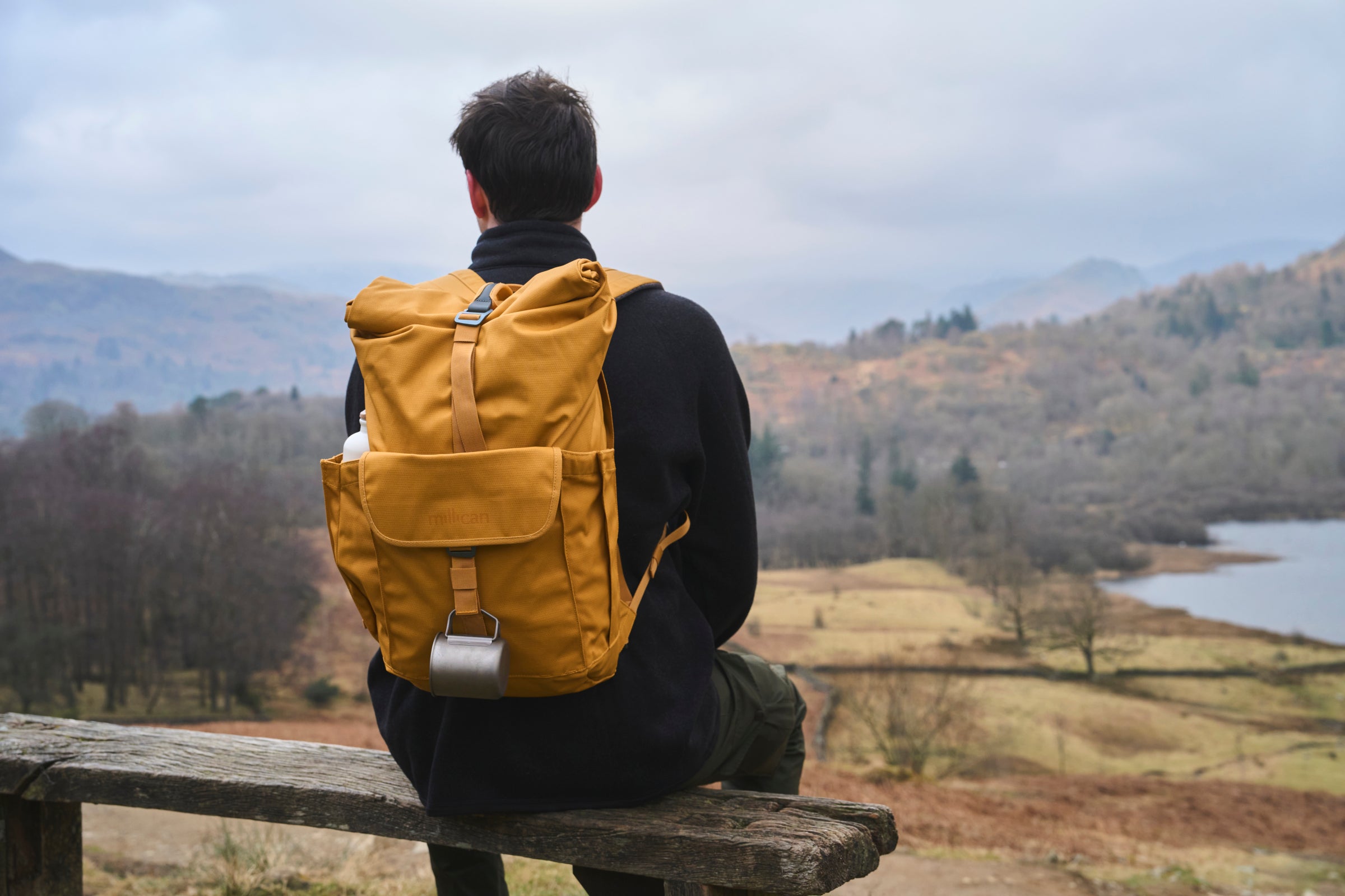 Person with a yellow backpack sitting on a bench overlooking a scenic landscape