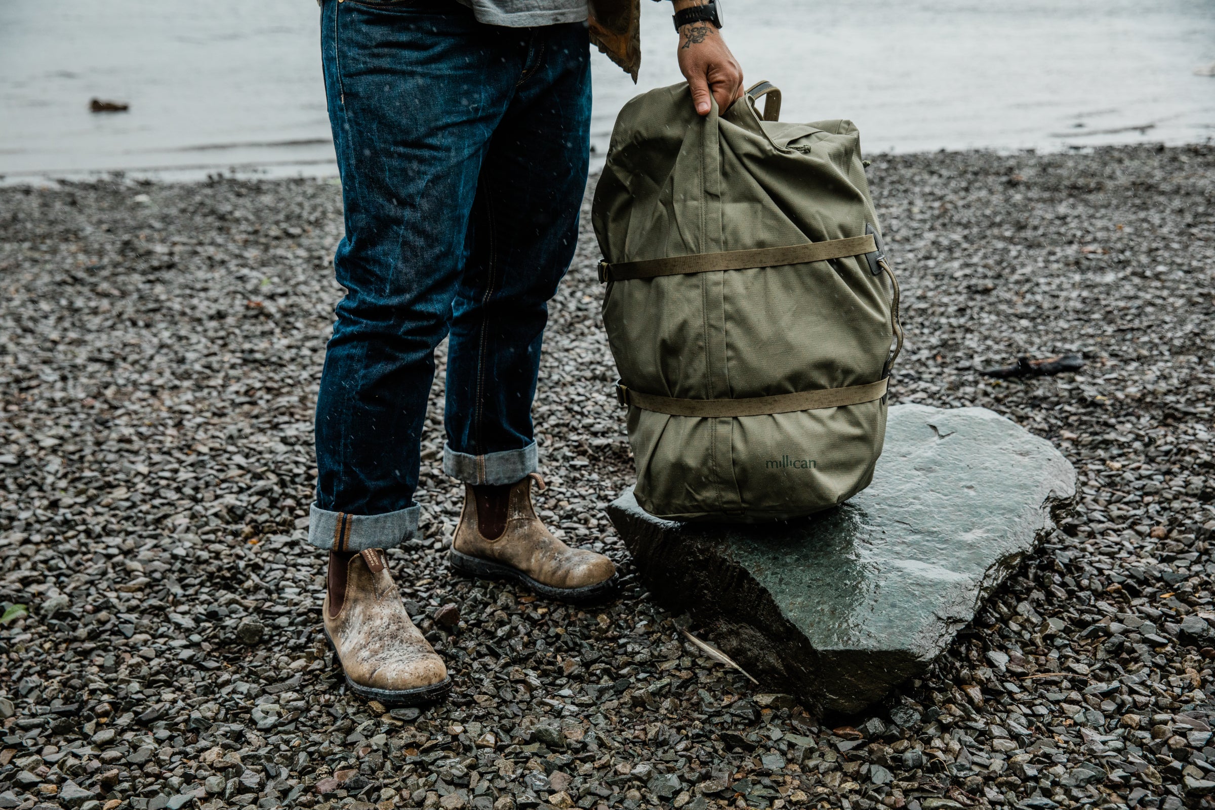 Person holding a green bag on a rocky lakeside